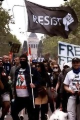 Dennis Basic, zijn gezicht verborgen door een zwarte bivakmuts, zwaait met een 'Resist'-vlag tijdens protesten tegen de lockdowns in Melbourne.