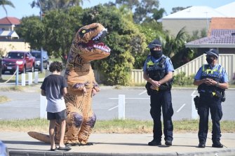One bystander wears a dinosaur suit next to police officers at a COVID presser in WA.