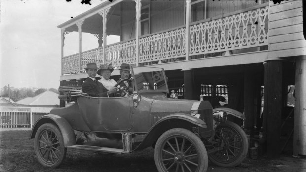 Three people in a single seat Ford car in front of a Queenslander style house with verandah taken by Queensland photographer Harriett Pettifore Brims.
