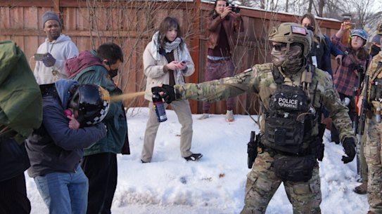 A law enforcement officer sprays a group of protesters with chemical spray at the scene of a shooting in Minneapolis.