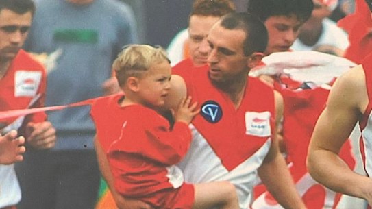 A three-year-old Tom Williamson is carried through the banner by his father Allister in 2001, the last time Ararat won a premiership.