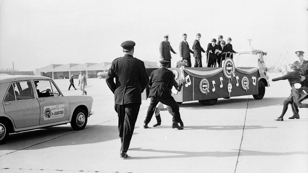 A policeman intercepts an over-enthusiastic fan as The Beatles look on, Mascot, Sydney, June 18, 1964.