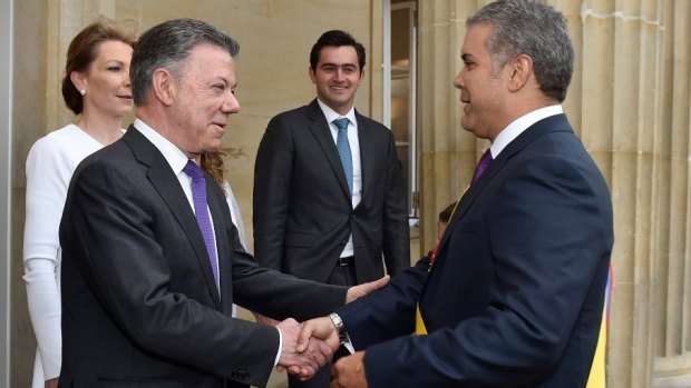 Colombia's outgoing President Juan Manuel Santos, left, welcomes newly sworn-in President Ivan Duque in Bogota, 