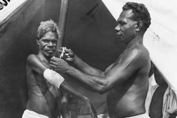 Orderly “Tommy” from the Australian General Hospital bandaging the arm of “Hector” who was injured when Katherine, NT, was bombed. Hector went bush, but later returned for treatment. November 24, 1942.
