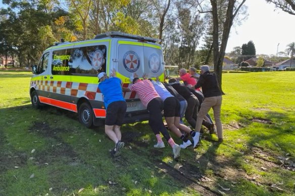 Bulldogs players push an ambulance out of the mud on a golf course. 