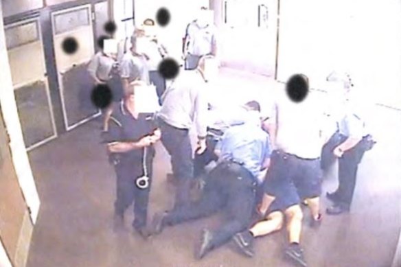 A still from CCTV footage of a young person being held on the ground was contained in a 2016 Queensland youth detention report that called for the practice to be banned.