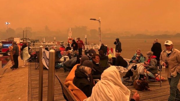 Locals and tourists on the Mallacoota wharf as fire devastated the region.