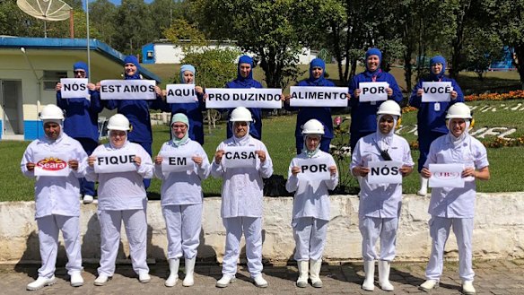 JBS Brazil employees pose with signs saying "We're here making food for you, stay home for us". In a statement, the company said it was committed to production operations "with great care to supply food in a time of need". 