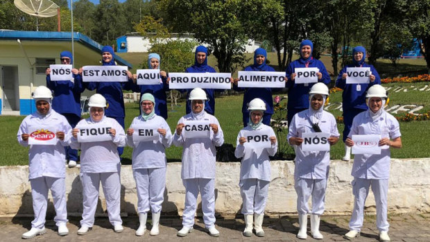 JBS Brazil employees pose with signs saying "We're here making food for you, stay home for us". In a statement, the company said it was committed to production operations "with great care to supply food in a time of need". 