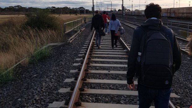 Passengers walk along the tracks after a train hit overhead cables
