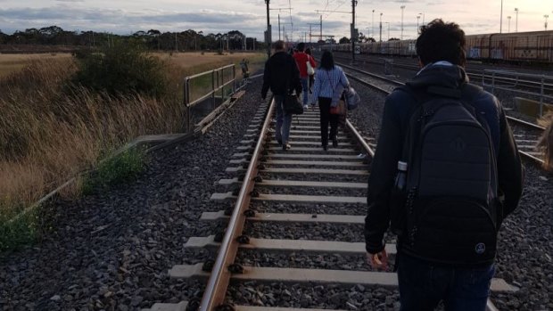 Passengers walk along the tracks after a train hit overhead cables.