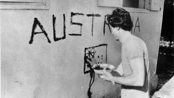 Greg Shackleton painting the word ’Australia” and a flag on the wall of a building in Balibo.