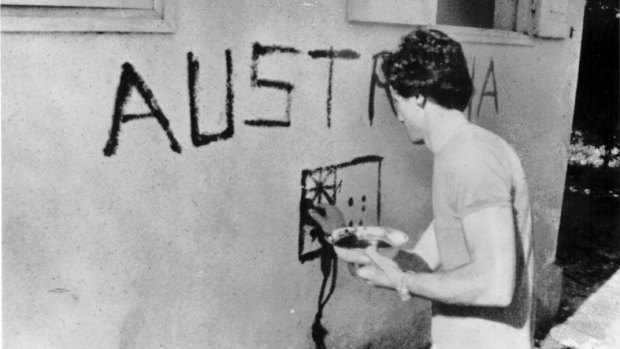 Greg Shackleton painting the word ’Australia” and a flag on the wall of a building in Balibo.