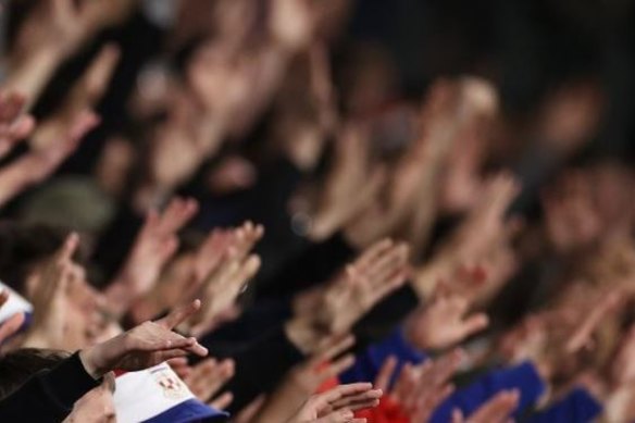 Sydney United fans at Allianz Stadium performing a popular chant in which their hands are raised.