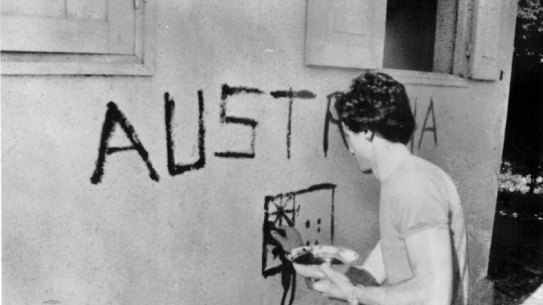 Greg Shackleton painting the word ’Australia” and a flag on the wall of a building in Balibo.