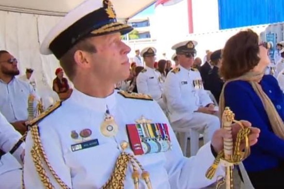 Vice-Admiral Michael Noonan in the foreground, and the dancers seated in their red and black costumes in the back row. 