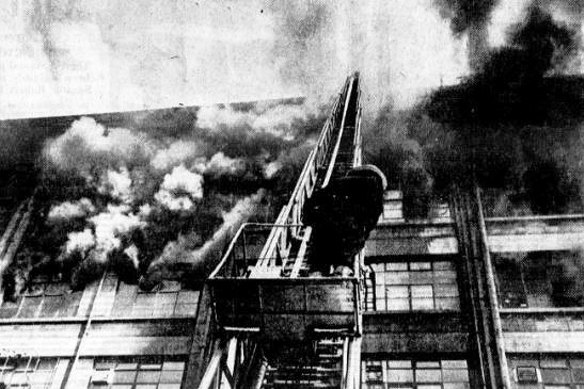 A fireman 'rides' an extension ladder toward the roof of the Mail Exchange building as heavy black smoke billows through broken windows.