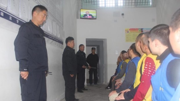 Detainees in Xinjiang watch a televised speech by a local politician as guards watch them in 2017.