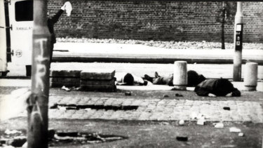 Scene from Bloody Sunday, January 30, 1972: Behind a lamp post with IRA chalked on it, a priest waves a white flag as ambulancemen dive for cover. 