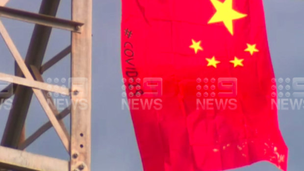 A Swastika symbol and two Chinese flags with COVID-19 written in black on them have been flown on a phone tower north of Melbourne. 
