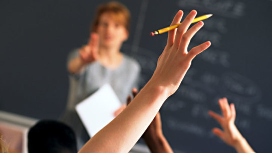 Teacher pointing to raised hands in classroom boarding school  Generic