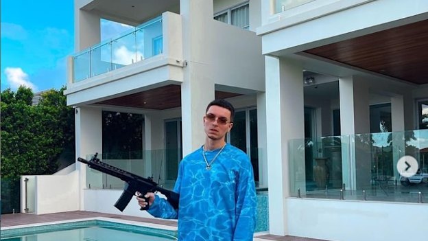 OnlyFans cryptocurrency ‘finfluencer’ Atis Paul shows off his designer duds and a firearm out the front of his Gold Coast home. 