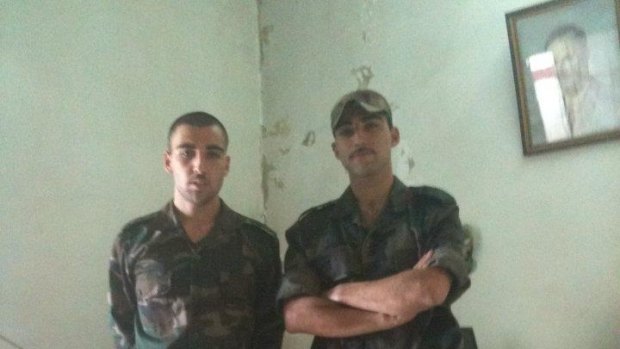Ali Ali (left) is pictured in military fatigues next to a portrait of Syrian dictator Bashar al-Assad's father, Hafez Al-Assad.