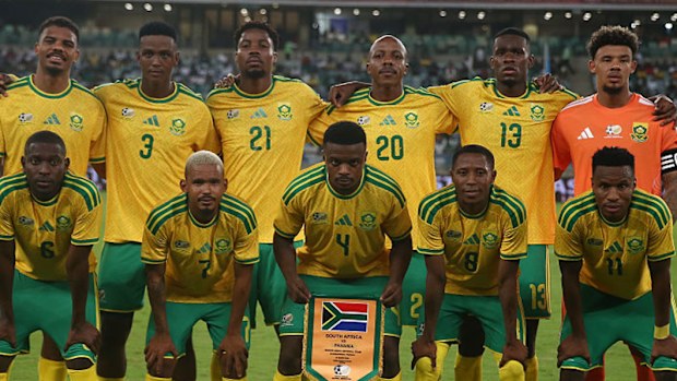 The South African men's football team pose for a photo on a football pitch. 