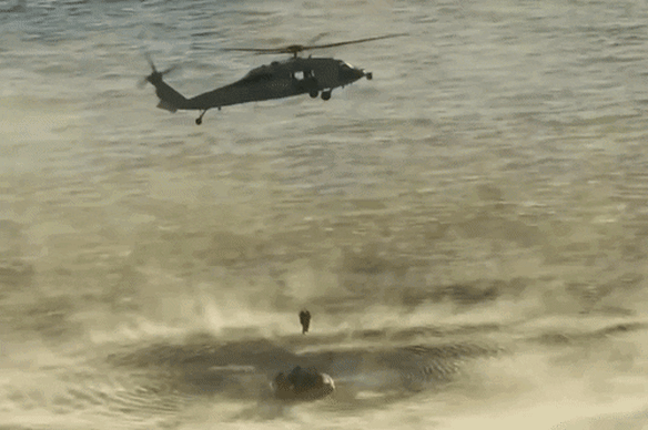 A military helicopter hoists an Artemis II astronaut to a waiting ship’s medical bay.
