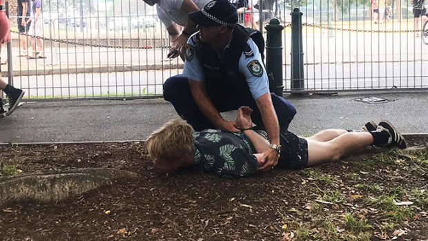 A NSW police officer pins a young man to the ground at the Field Day festival.