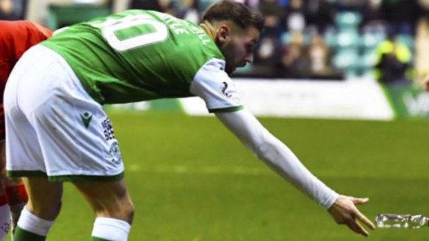 A Hibs player removes a glass bottle thrown at Borna Barisic from the crowd.