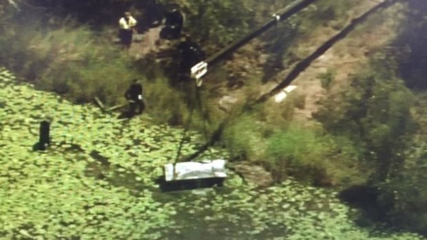 A crane lifts the metal toolbox containing the two bodies from a dam in Logan.