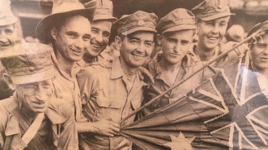 Wal Williams on the right smiling behind the flag.