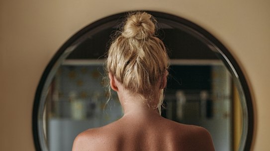 Blonde woman standing in front of the bathroom mirror in the morning.