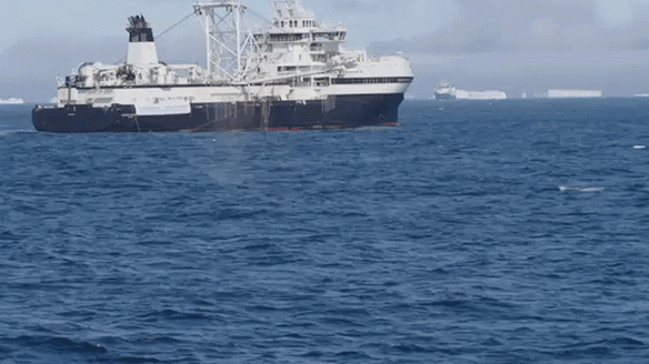 A whale breaches in the Antarctic near a krill trawler.