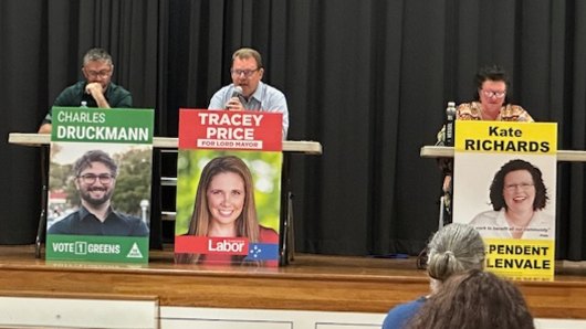 LNP councillor Greg Adermann sits behind a corflute with Tracey Price’s name on it.