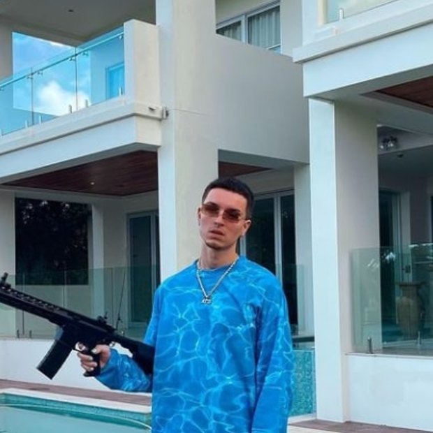 OnlyFans cryptocurrency ‘finfluencer’ Atis Paul shows off his designer duds and a firearm out the front of his Gold Coast home. 