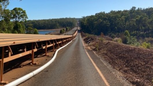 The unsecured PFAS pipeline meanders onto a road next to a bauxite conveyor.