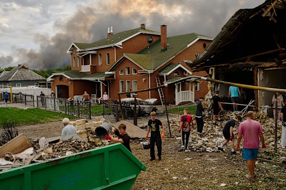 Local residents remove debris from a heavily damaged house as smoke rises from a destroyed warehouse, in the background, after Russian drone attacks on the outskirt of Kyiv, Ukraine.