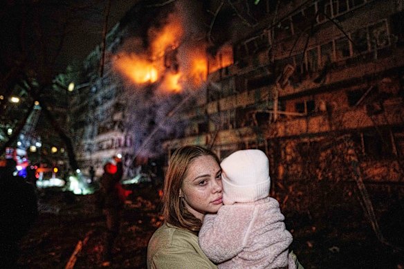 Victoria Deineko holds her daughter, Mia, in front of a multi-story residential building damaged in a Russian missile strike in Kyiv onTuesday.