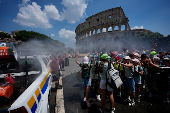 People seek relief under a water-sprinkling cannon for tourists visiting the Colosseum and Roman Forum.