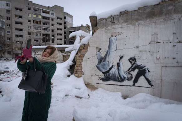 A woman takes a selfie at an artwork that was made by British street artist Banksy on a building destroyed by the Russian army in Borodyanka, Kyiv region, Ukraine in 2022. 