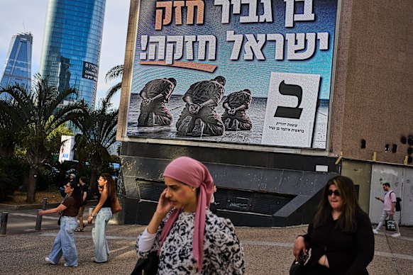 People walk past an election campaign billboard for National Security Minister Itamar Ben-Gvir in Ramat Gan, depicting handcuffed Palestinian prisoners and a Hebrew slogan reading, “Strong Ben-Gvir, Strong Israel”.