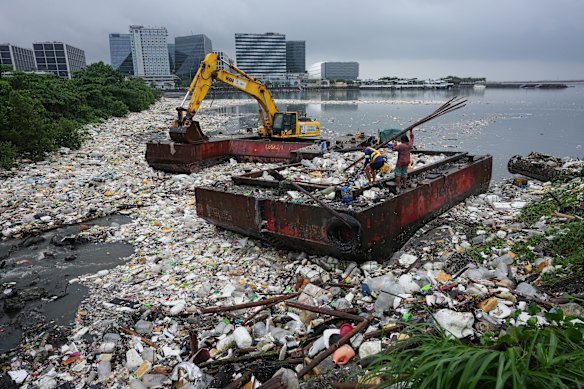 Workers carry bamboo beside a sea of garbage that was washed ashore due to intense monsoon rains in Pasay city, Metro Manila, Philippines.