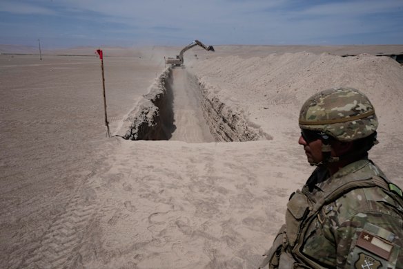 A soldier stands near a machine digging along the northern border at the Chacalluta border crossing, in Arica, Chile.
