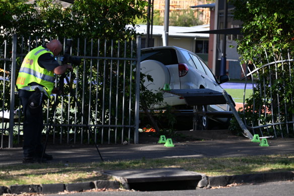 A detective photographs the car after it ploughed through the fence at Auburn South Primary School.