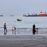 People spend time at a beach as commercial vessels are anchored in the Strait of Hormuz off Bandar Abbas, Iran.