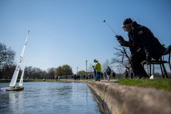 Un homme portant un masque facial exploite un bateau télécommandé sur un étang à Clapham Common à Londres.  Le gouvernement britannique a assoupli les règles de socialisation, permettant à des groupes de six personnes (ou plus si limité à deux ménages) de se rencontrer à l'extérieur.