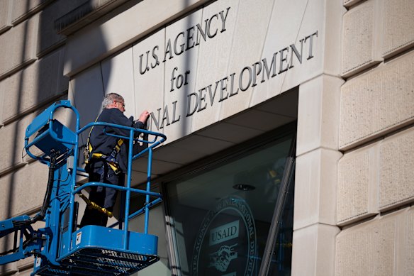 A worker removes the US Agency for International Development sign from its Washington headquarters after DOGE shut it down this year.