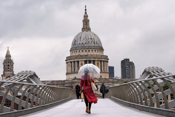 A pedestrian holds an umbrella as she walks over the Millennium Bridge in London.
